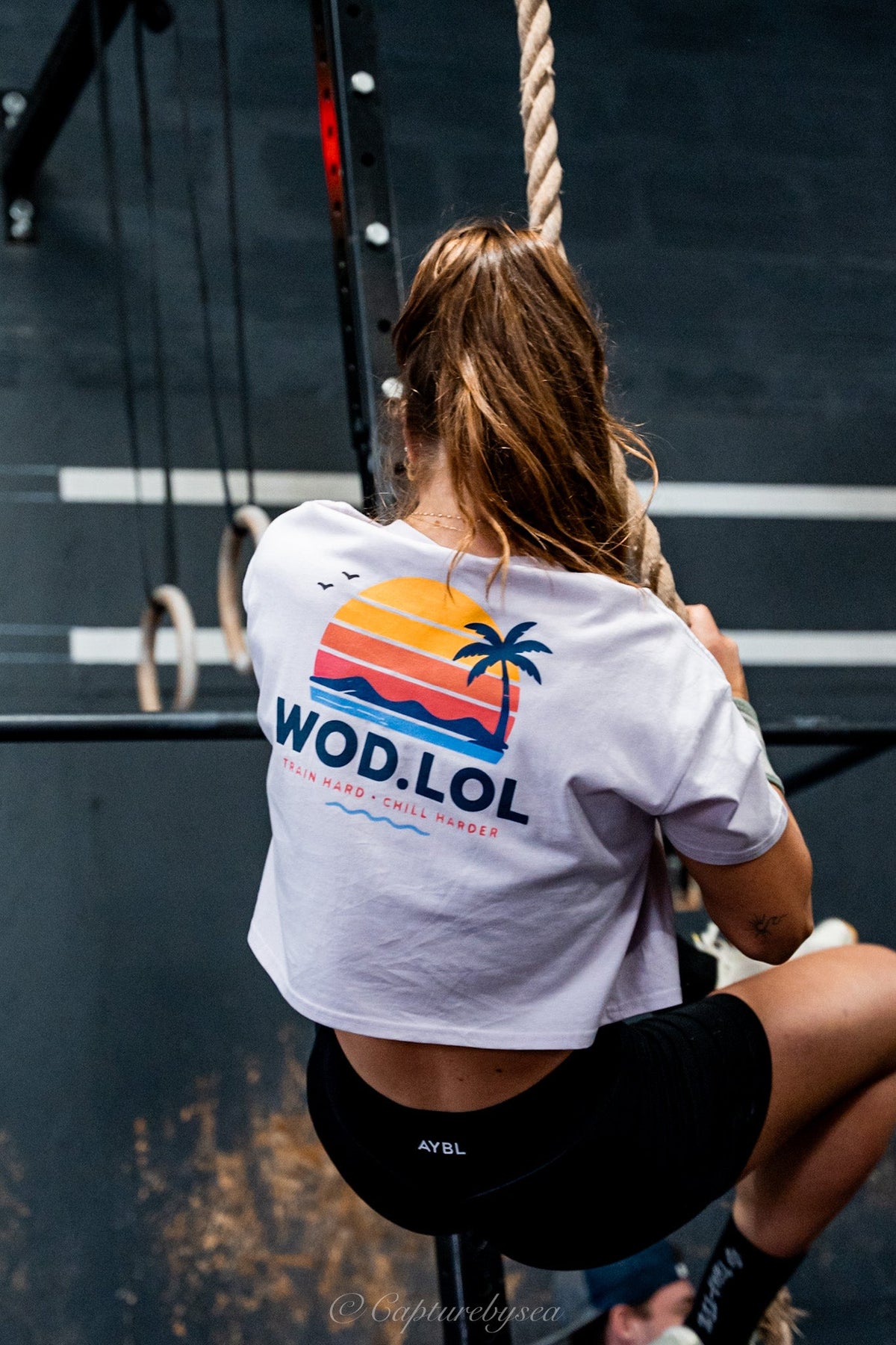 Femme en montée de corde portant le crop top WOD.LOL Summer Co. 2026, imprimé coucher de soleil et palmier – WOD.LOL